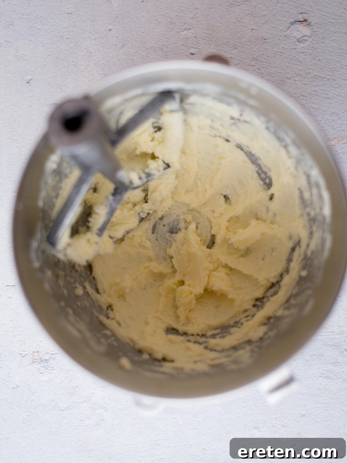 Butter and granulated sugar being creamed together in a large white mixing bowl, showing a light and fluffy texture
