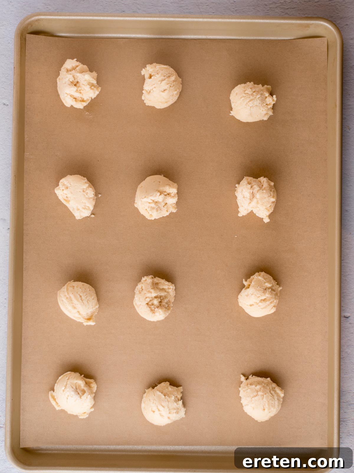 Scooped balls of condensed milk cookie dough evenly spaced on a parchment-lined baking sheet, ready for the oven