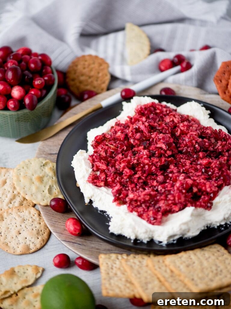 Sweet Heat Cranberry Jalapeño Dip 2 A vibrant cranberry jalapeno dip layered over smooth cream cheese, served on a white platter with crackers.