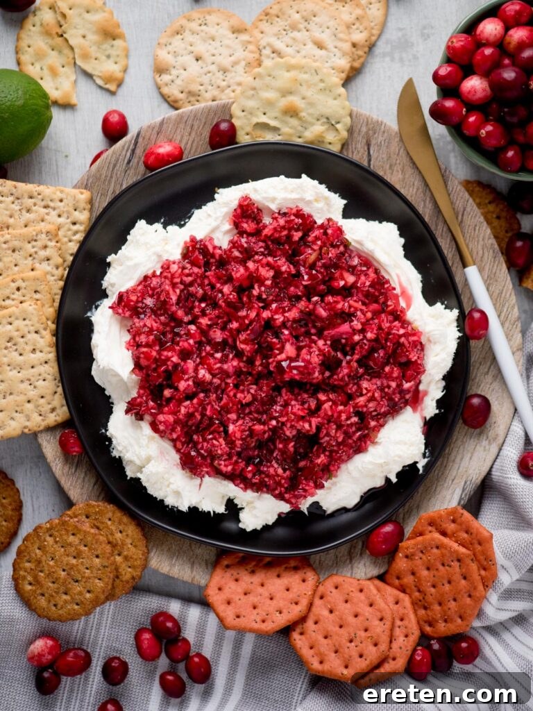Sweet Heat Cranberry Jalapeño Dip 9 Overhead view of a prepared cranberry jalapeno dip with whipped cream cheese, surrounded by an assortment of crackers on a white surface.