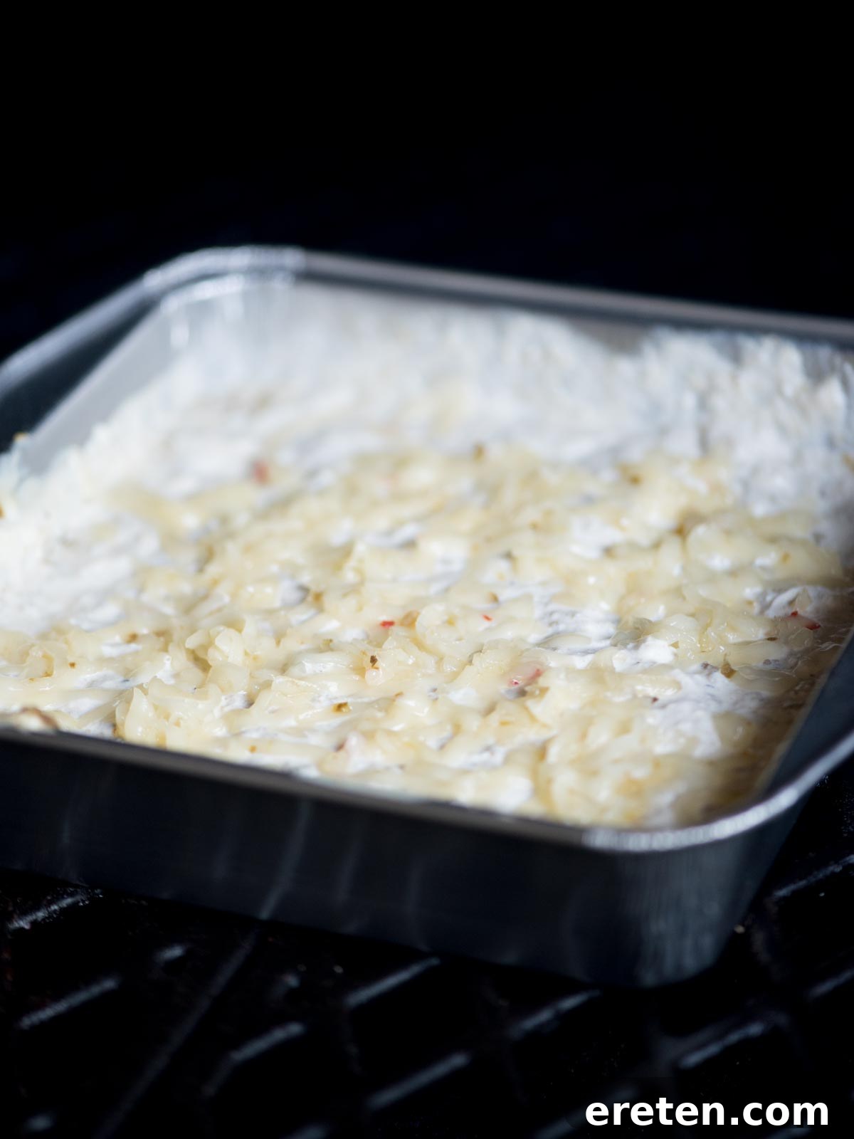 A baking dish of queso blanco placed inside a smoker, with a gentle wispy smoke visible.