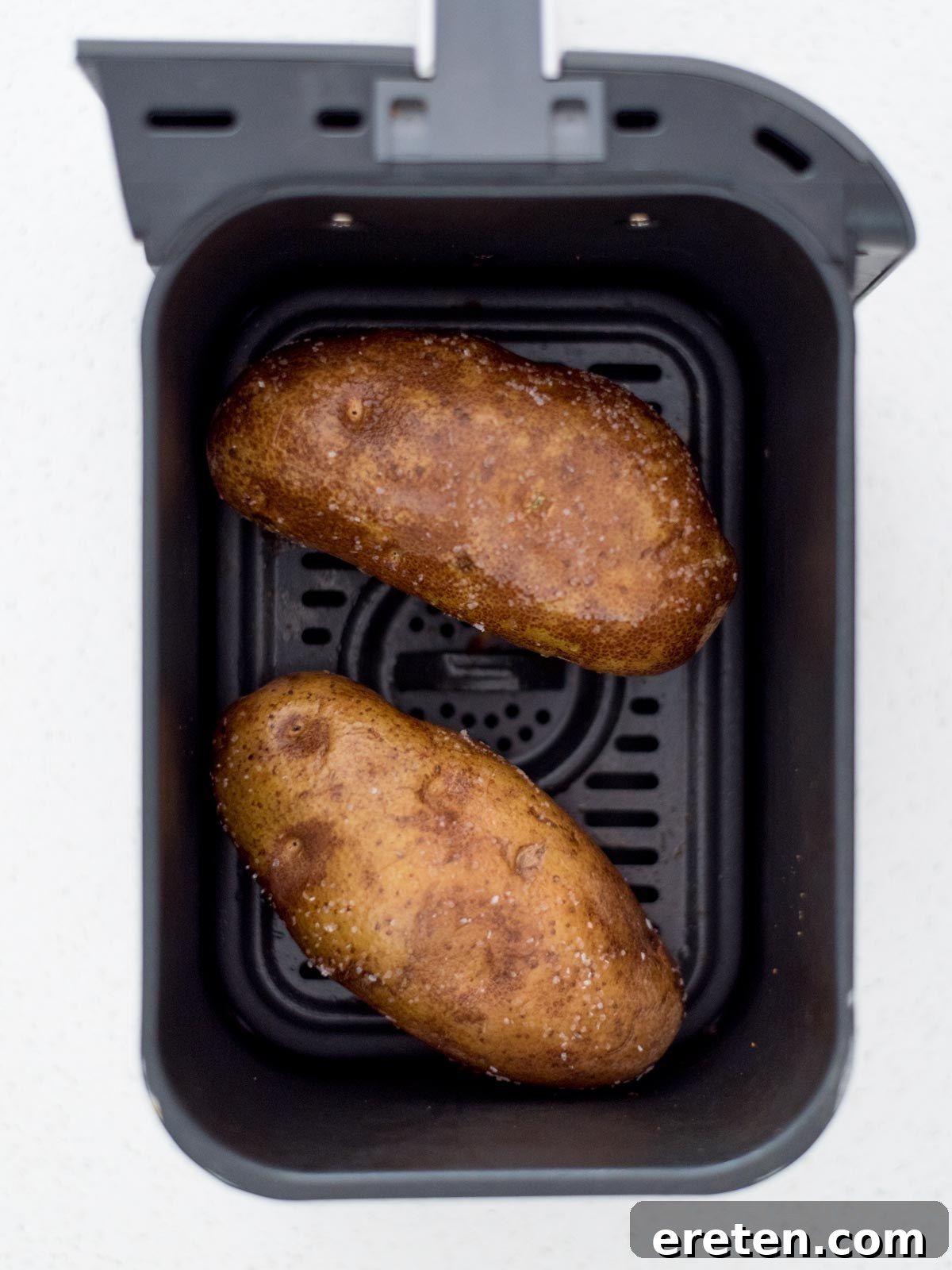 Two whole potatoes inside an air fryer.
