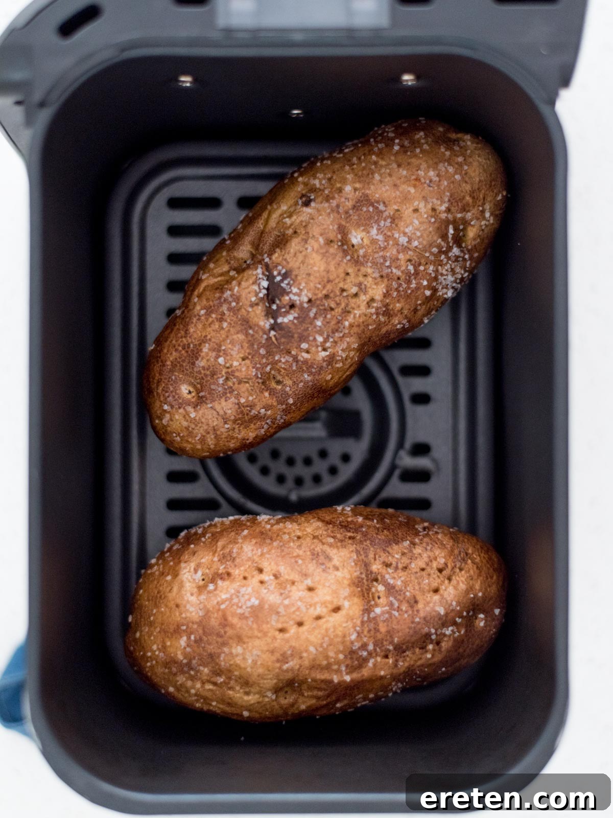 Two potatoes with salt and oil rubbed on them in an air fryer.
