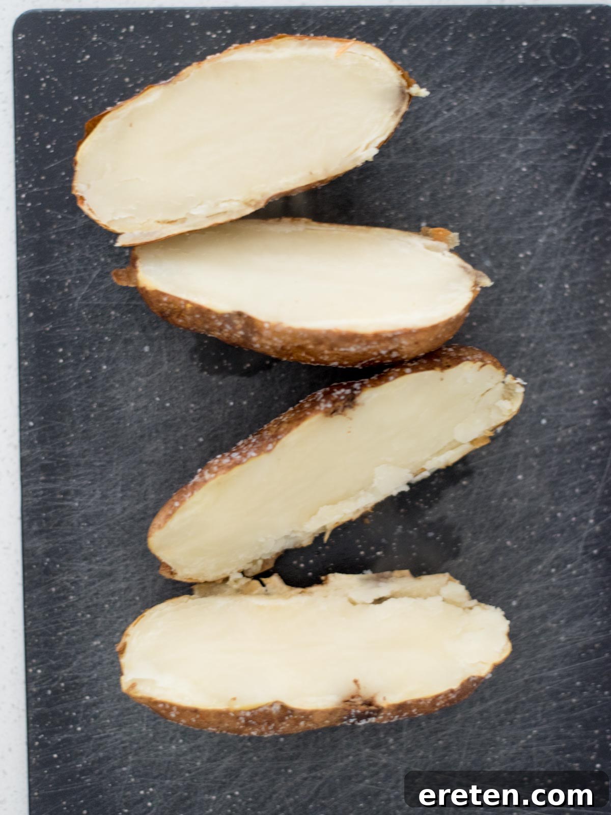 Cooked potatoes cut in half on a cutting board.