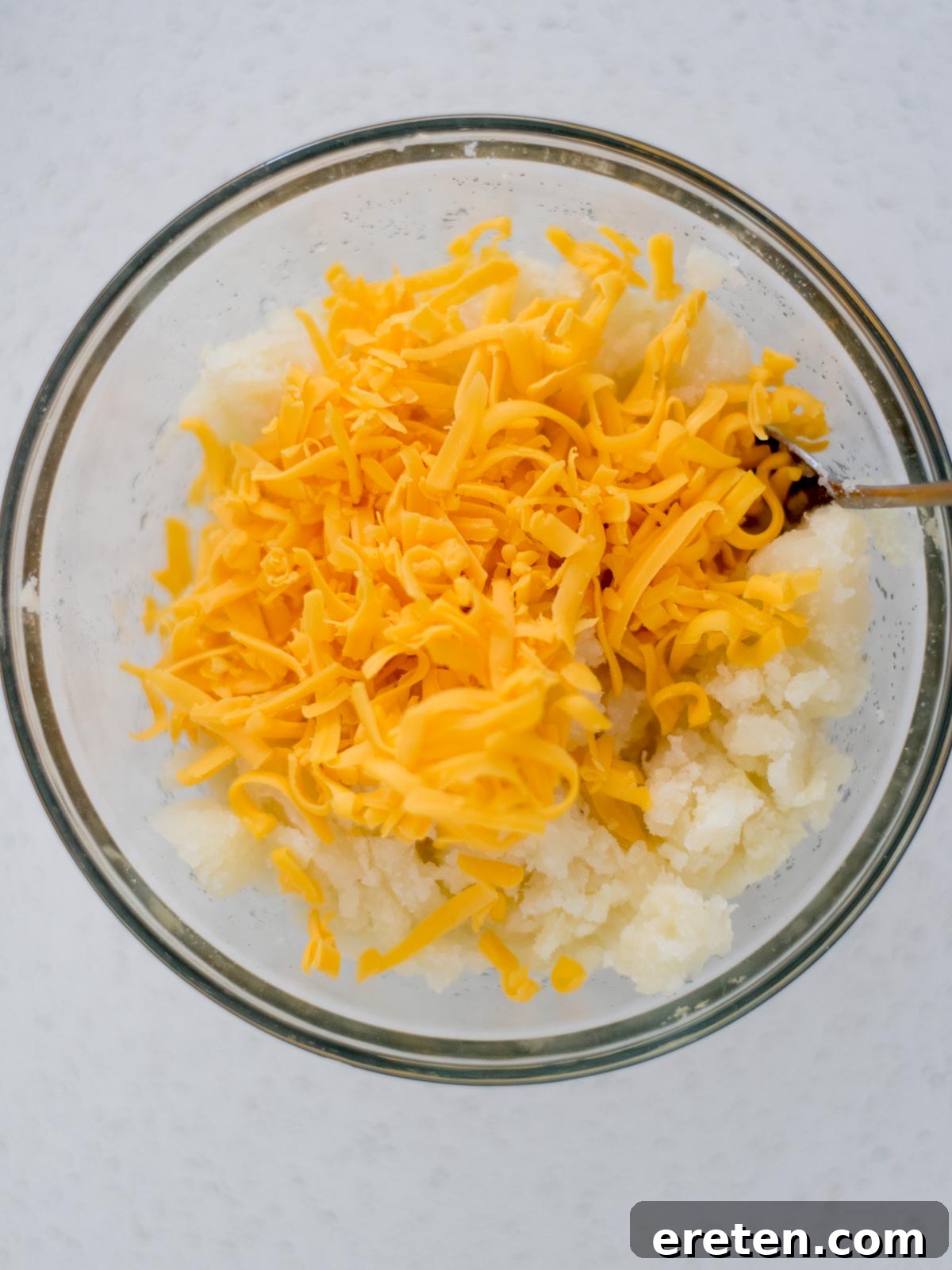 Potatoes and shredded cheese added to a mixing bowl for twice baked potatoes.