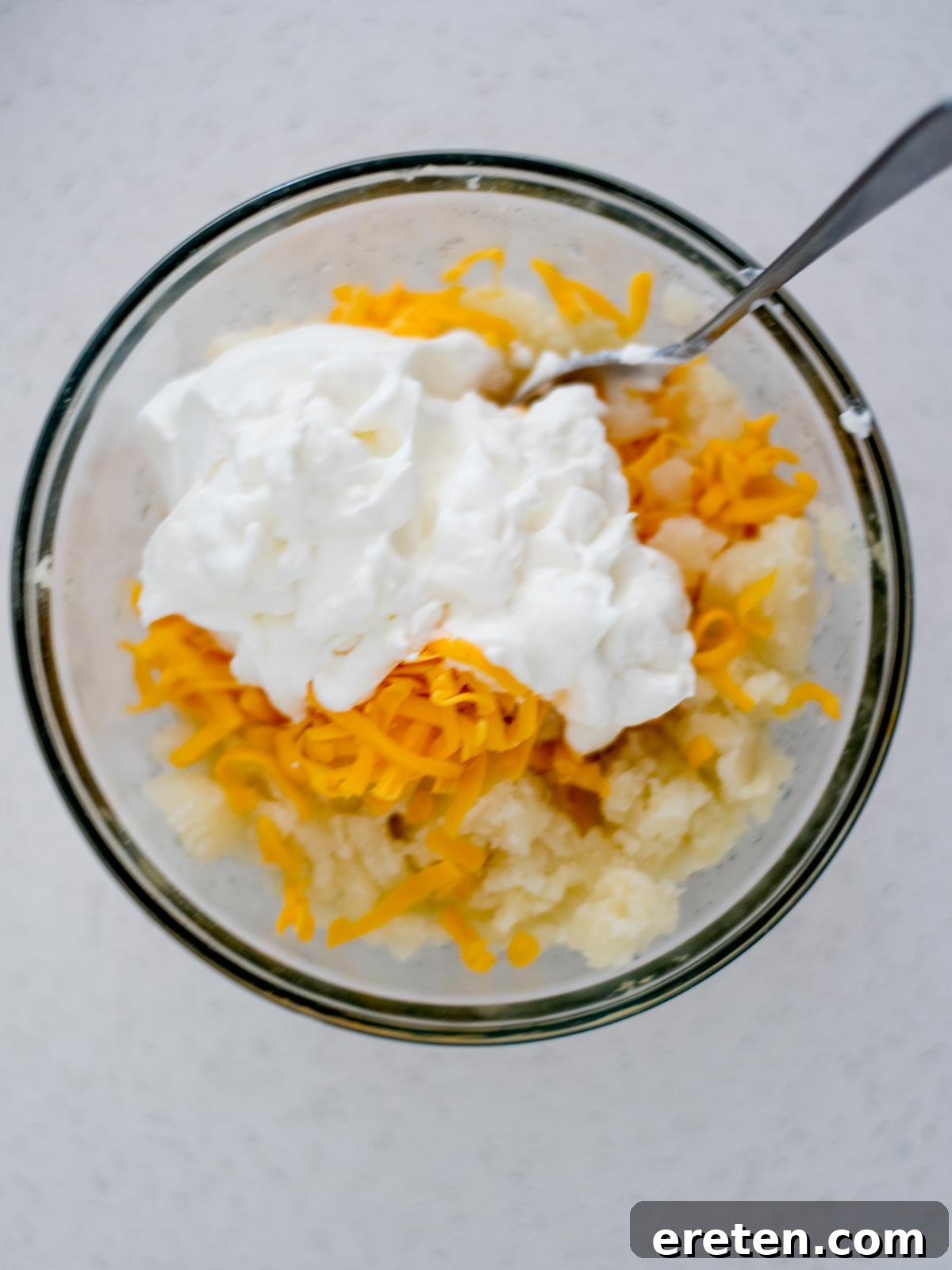Potatoes, shredded cheese and sour cream added to a mixing bowl for twice baked potatoes.