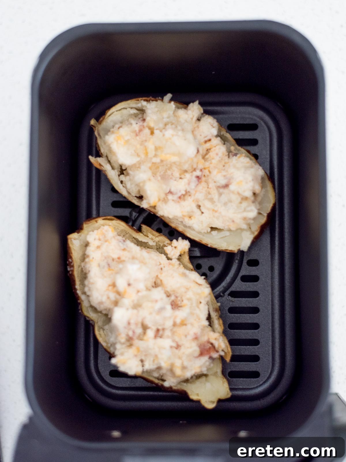 Two twice baked potatoes with the filling inside the potato skins sitting inside the air fryer.