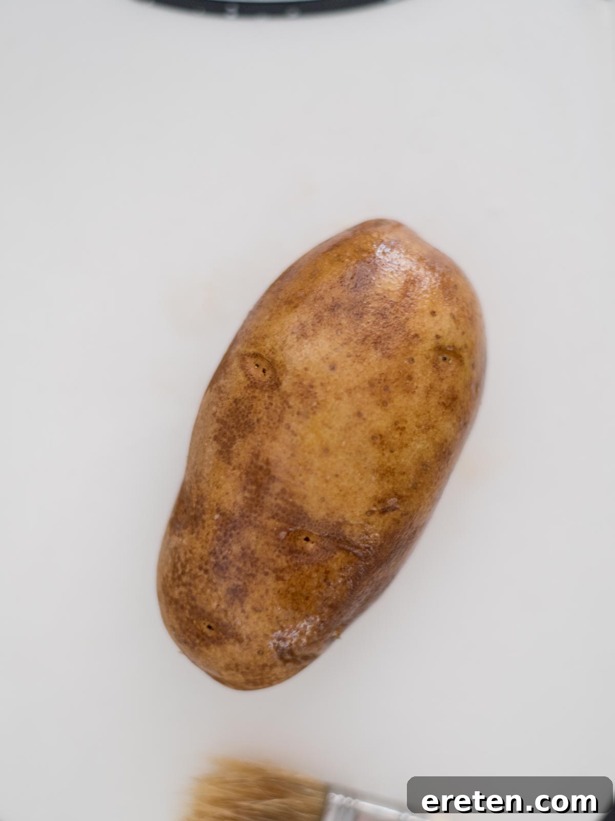 A washed whole potato poked with the tines of a fork.