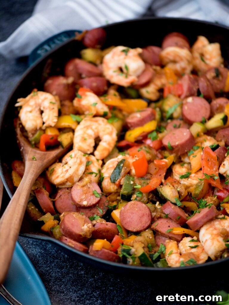 Cajun Fire Skillet with Shrimp and Sausage 9 Wooden spoon holding a scoop of cajun shrimp and sausage with vegetables in a cast iron pan.