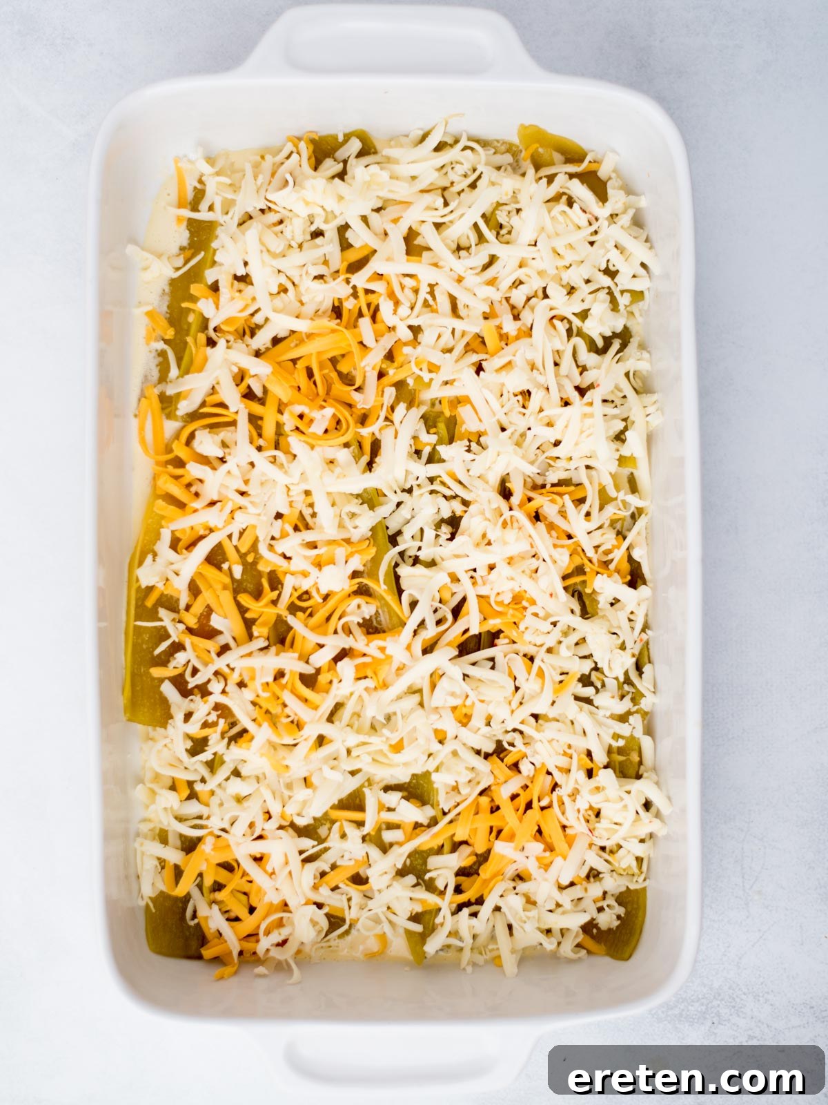 Shredded cheese generously added to the top of the hatch chiles, preparing for the next layer.