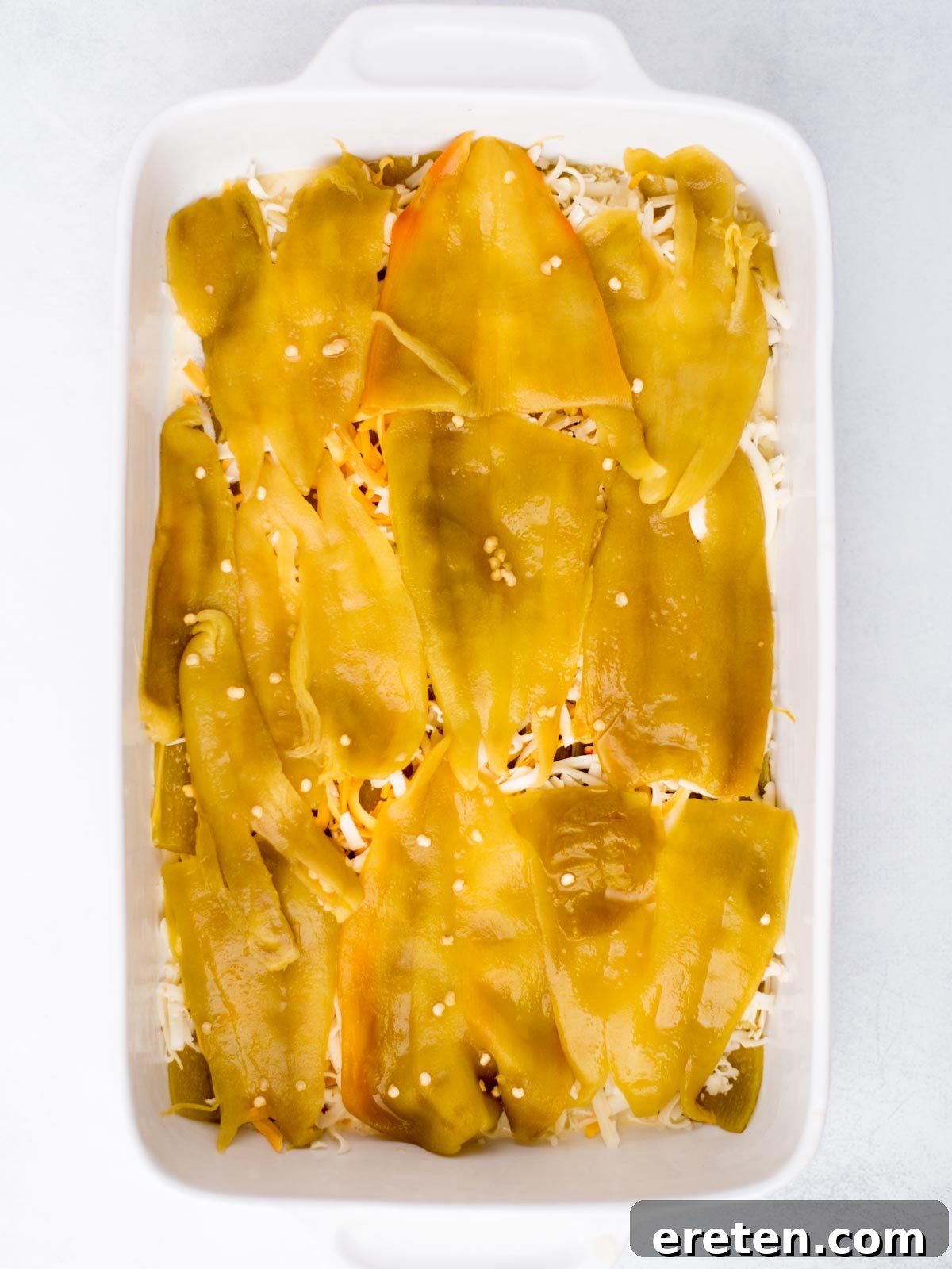 Second layer of hatch chiles added to the shredded cheese in the baking dish, building up the casserole.