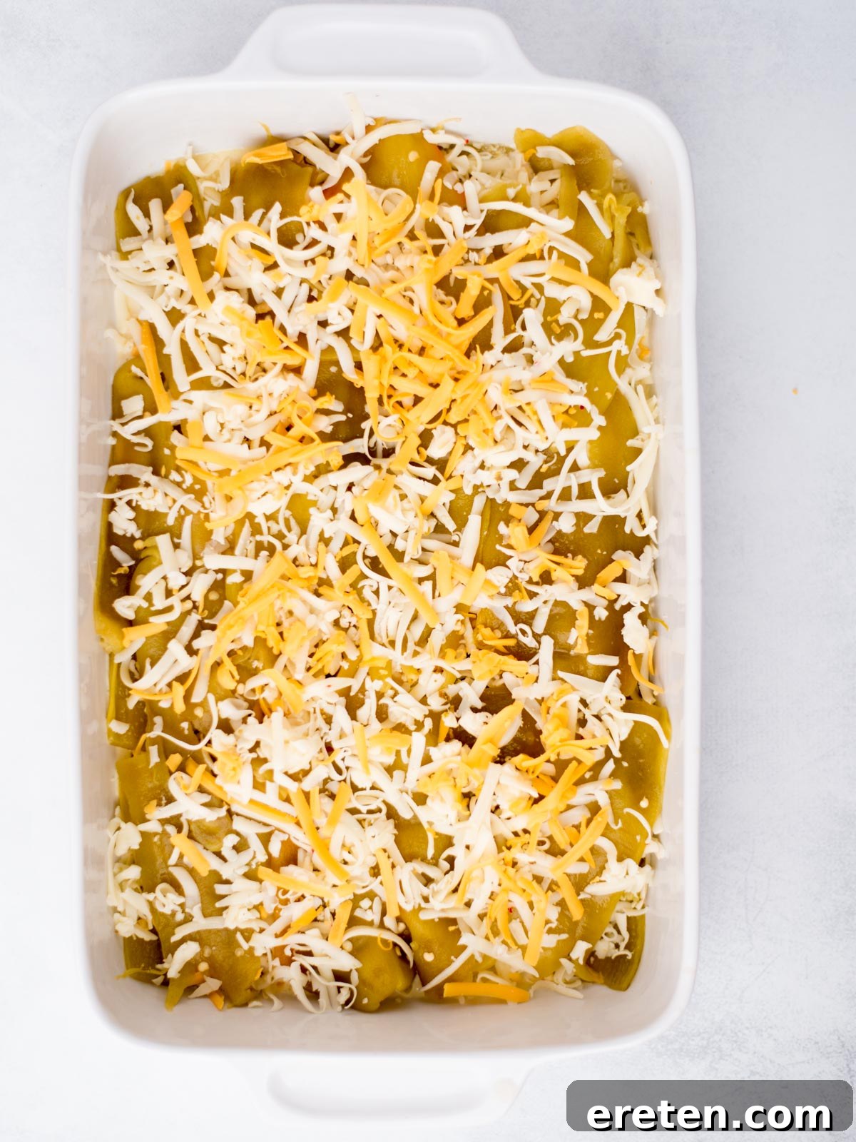 Casserole baking dish with egg mixture, hatch chiles and shredded cheese layered in it, ready for the final egg pour.