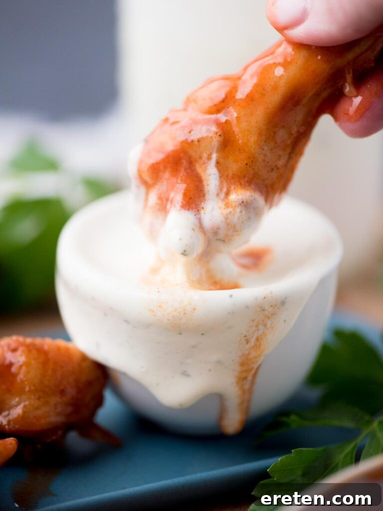 Hand dunking a crispy chicken drumstick into a small bowl of creamy homemade Wing Stop Ranch dressing.