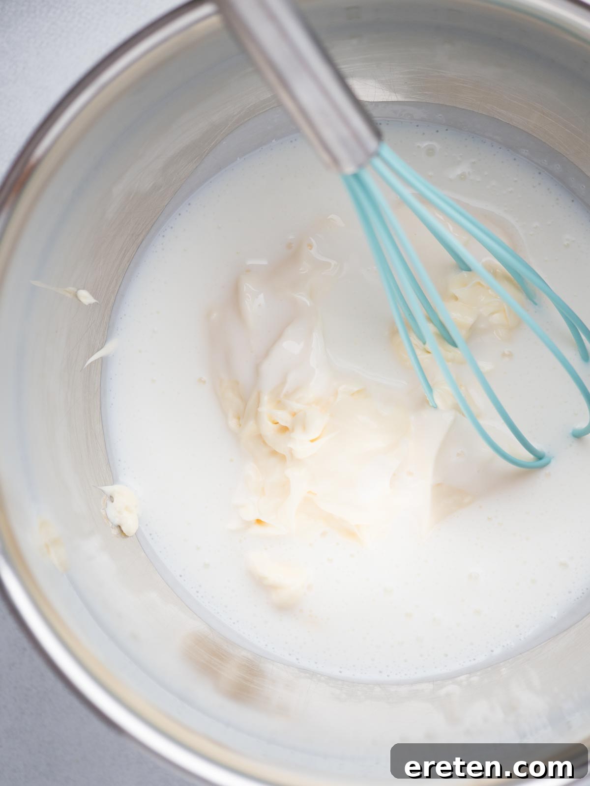 A mixing bowl with measured buttermilk and mayonnaise, with a whisk resting inside, ready for mixing.