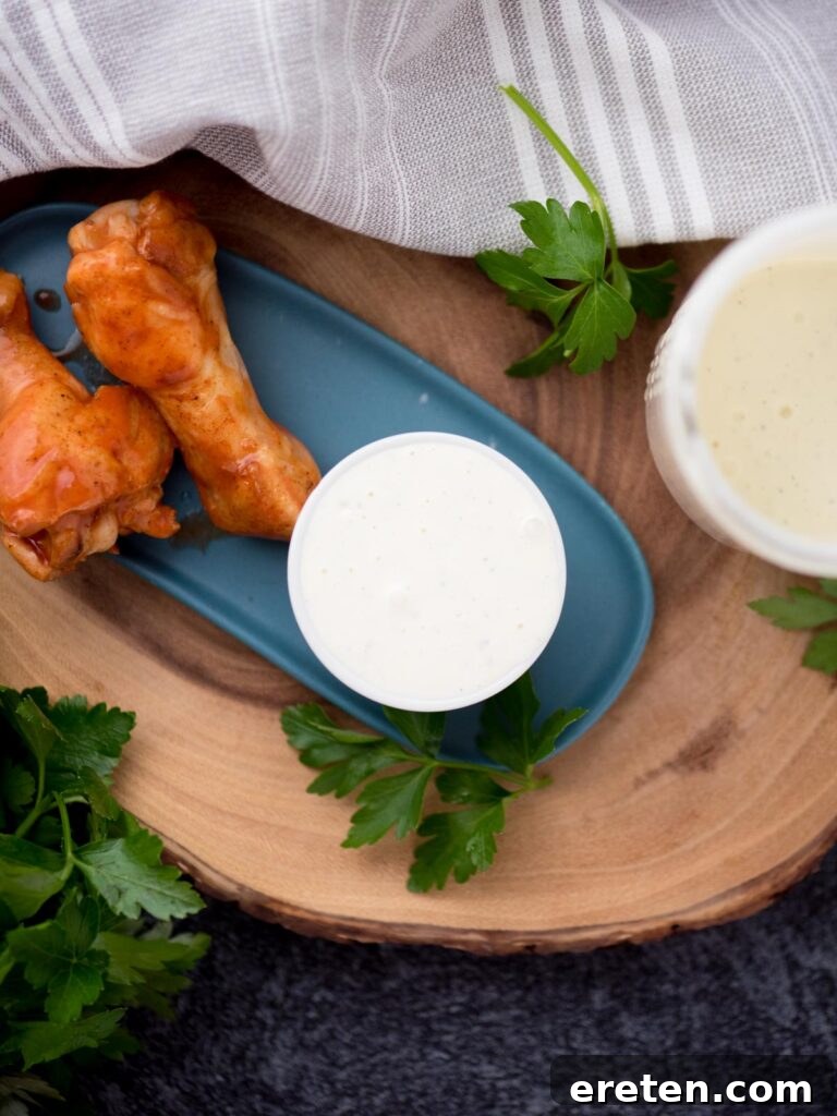 Crispy chicken drumsticks on a plate, alongside a small bowl of creamy Wing Stop Ranch garnished with fresh cilantro leaves.