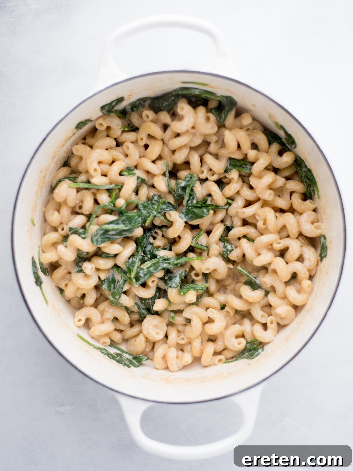 Cooked pasta mixed with wilted spinach in a dutch oven.