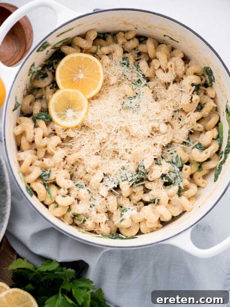 Top view of a dutch oven with parmesan cheese over lemon ricotta pasta, garnished with lemon slices.