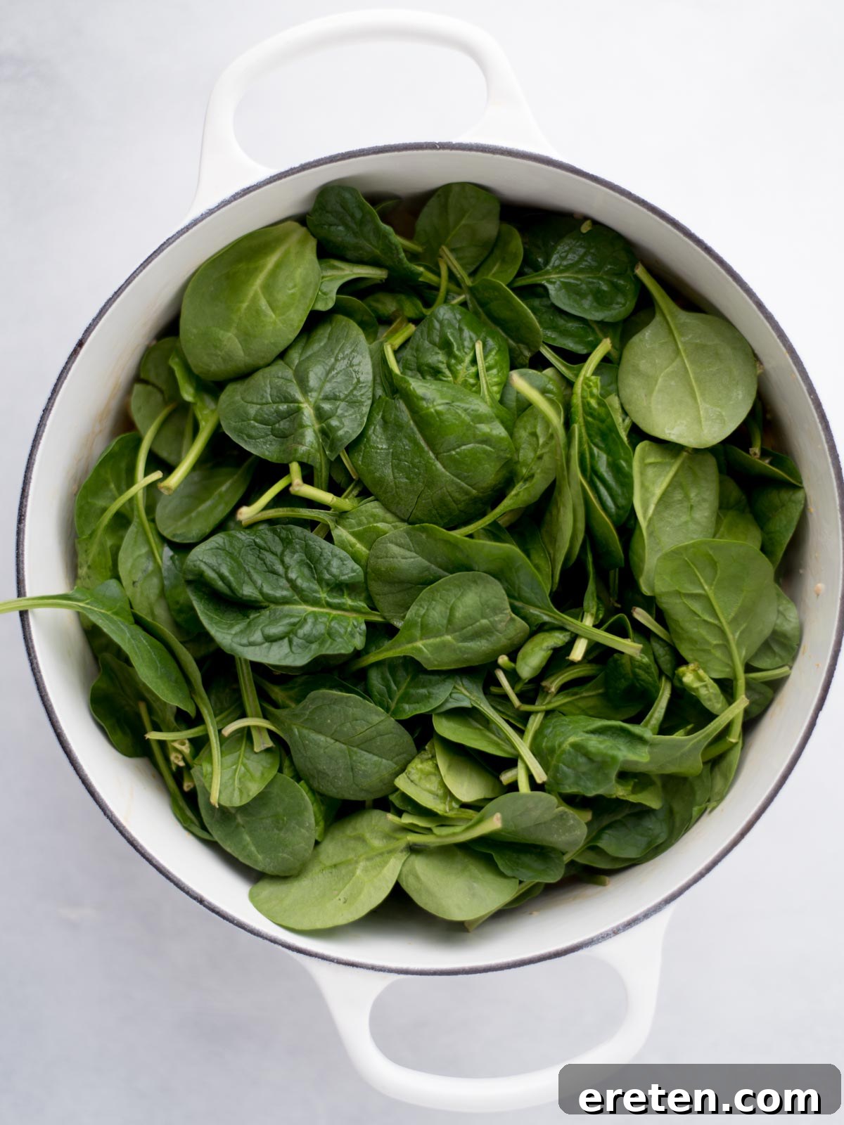 Dutch oven filled with fresh spinach leaves.