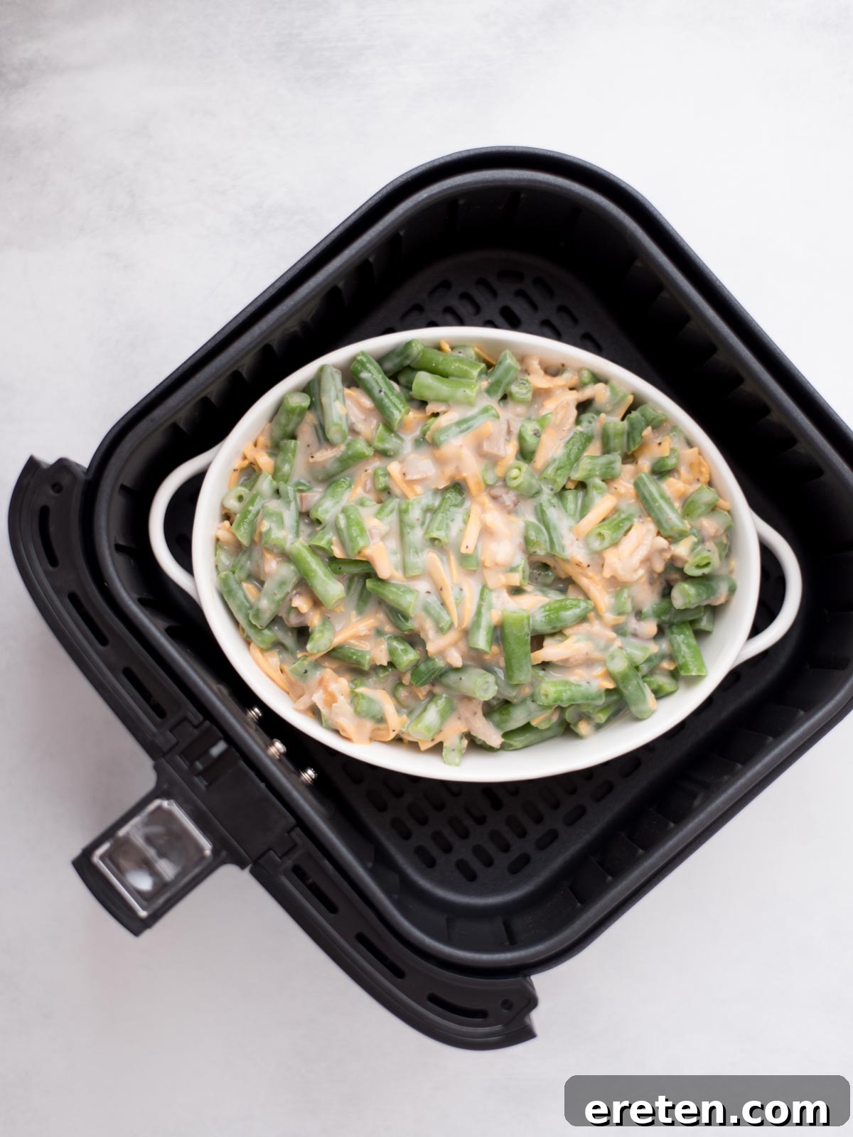 Baking dish in the air fryer filled with green bean casserole ready to cook.