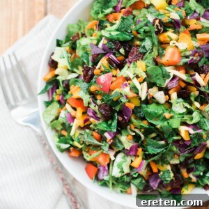 A vibrant green salad with assorted vegetables in a white bowl, dressed with vinaigrette.