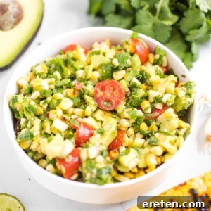 A colorful summer corn salad featuring corn, avocado, and tomatoes in a white bowl.