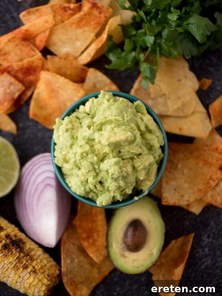 An overhead shot of a bowl of four-ingredient guacamole, surrounded by tortilla chips, with a half avocado and red onion for garnish, showcasing its fresh appeal.