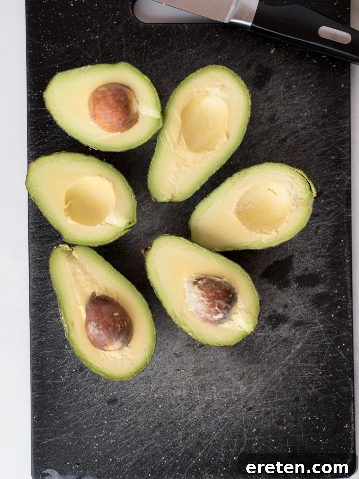 Two perfectly halved avocados, revealing their smooth green flesh and central seed, ready for pitting.