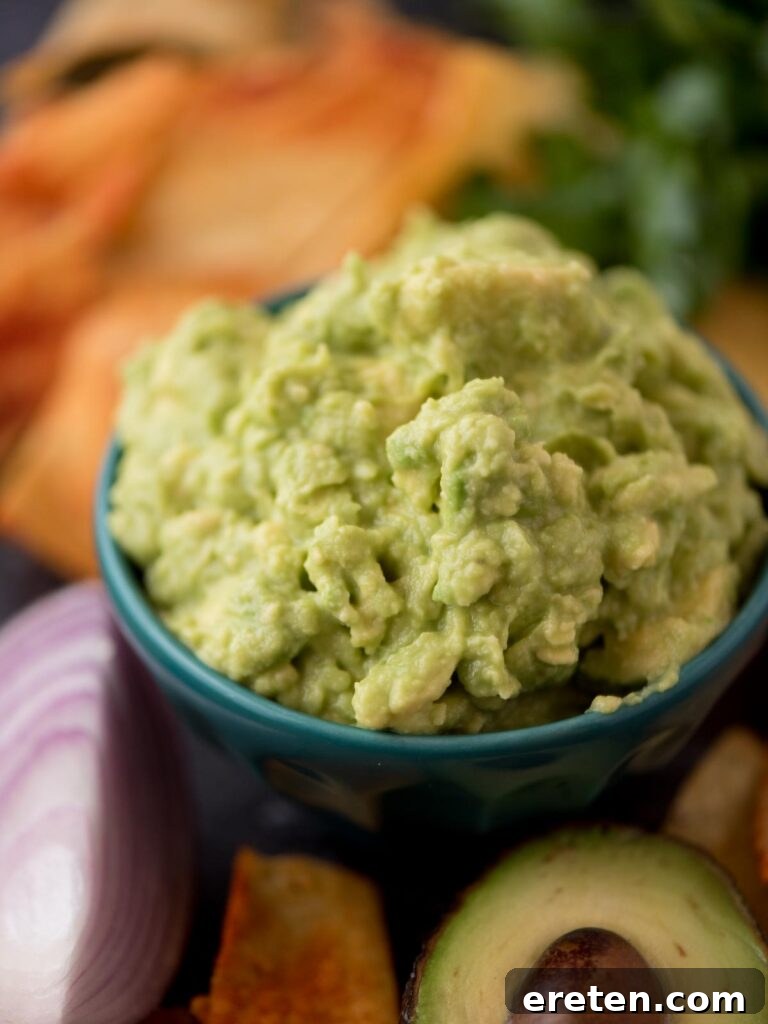 A small bowl of creamy four-ingredient guacamole sits next to a halved avocado and a vibrant red onion, inviting a delicious tasting.