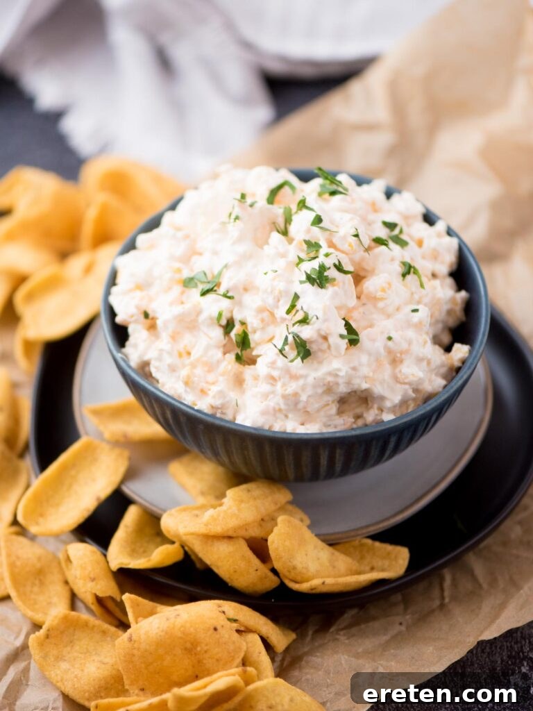 Vibrant corn dip with cream cheese in a blue ceramic bowl, garnished with fresh chopped parsley, and surrounded by crispy corn chips, ready for serving.