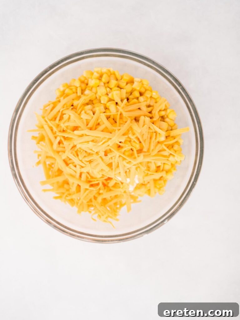 A large mixing bowl filled with all the ingredients for corn dip, including corn kernels, shredded cheese, and creamy base, ready to be mixed together.