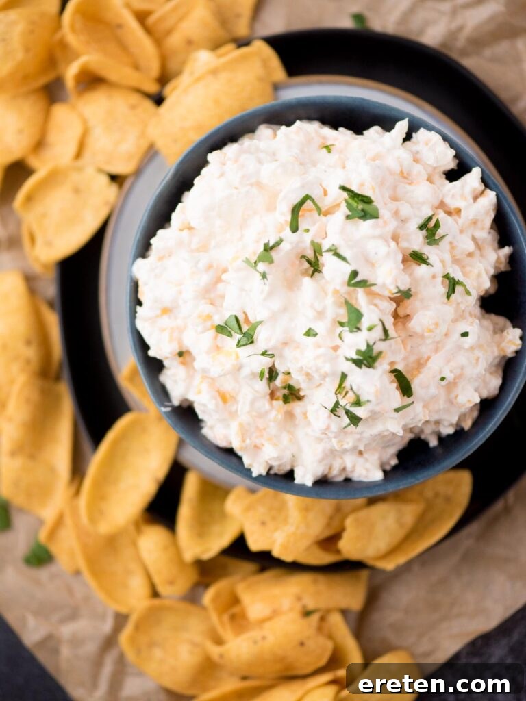 Creamy corn dip in a vibrant blue bowl, generously sprinkled with fresh green parsley, surrounded by a scattering of perfectly scooped corn chips, ready for a party.