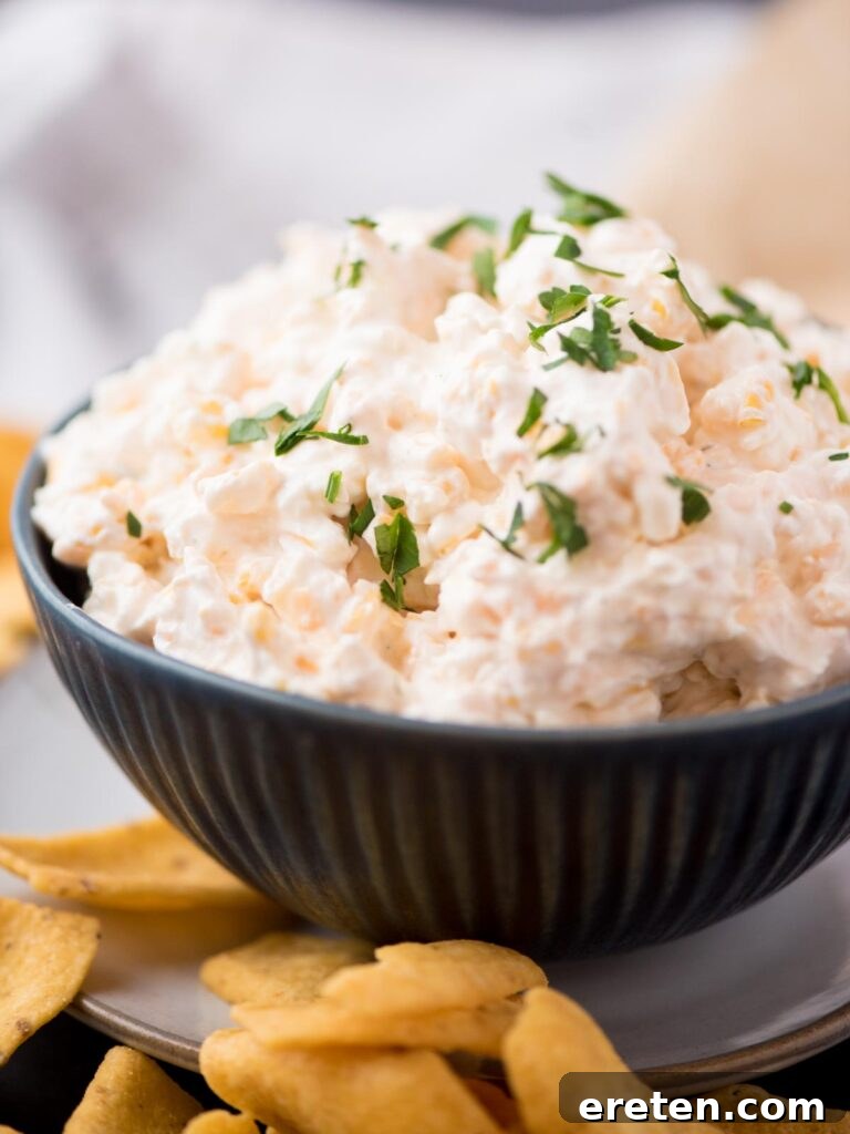 Close-up of creamy corn dip with cream cheese in a deep blue bowl, garnished with fresh chopped parsley, and surrounded by a generous amount of crunchy corn chips.