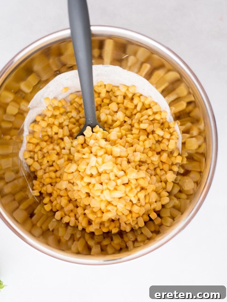 Fiesta Corn Bake 6 Thawed corn kernels being added to the creamy street corn casserole sauce in a mixing bowl.