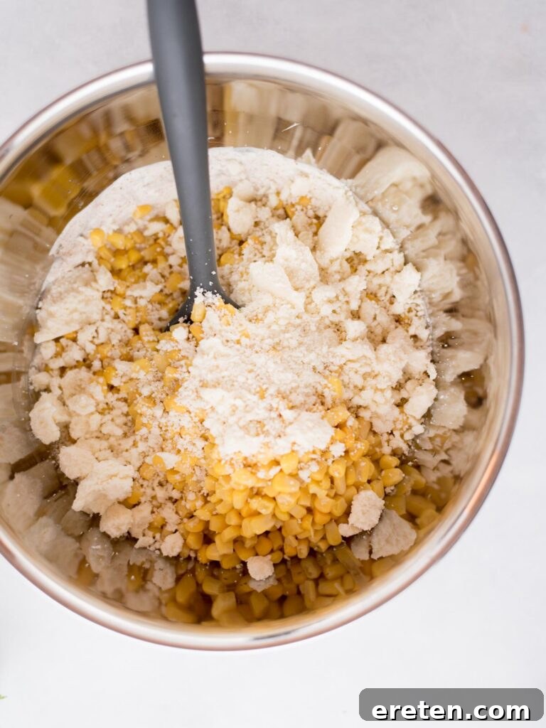 Fiesta Corn Bake 7 A mixing bowl with corn and cotija cheese being stirred into the sauce with a spoon.