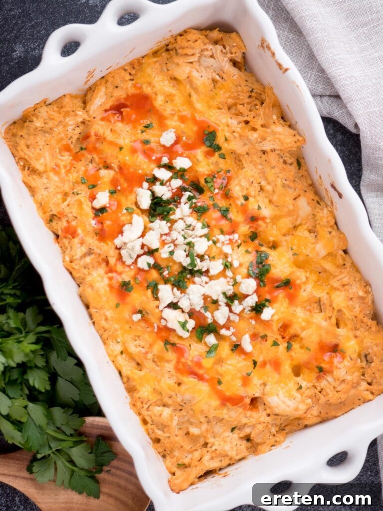 Close-up of a serving of creamy buffalo chicken dip topped with green onions and a drizzle of buffalo sauce, ready to be served with tortilla chips.