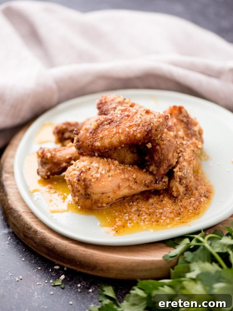 Air-Fried Golden Garlic Parmesan Wings 2 Crispy garlic parmesan chicken wings stacked on a light blue plate, garnished with fresh parsley