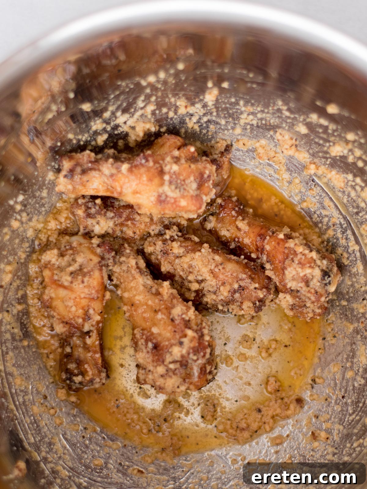 Air-Fried Golden Garlic Parmesan Wings 12 Cooked wings fully coated in garlic parmesan sauce, glistening and ready to serve in a mixing bowl