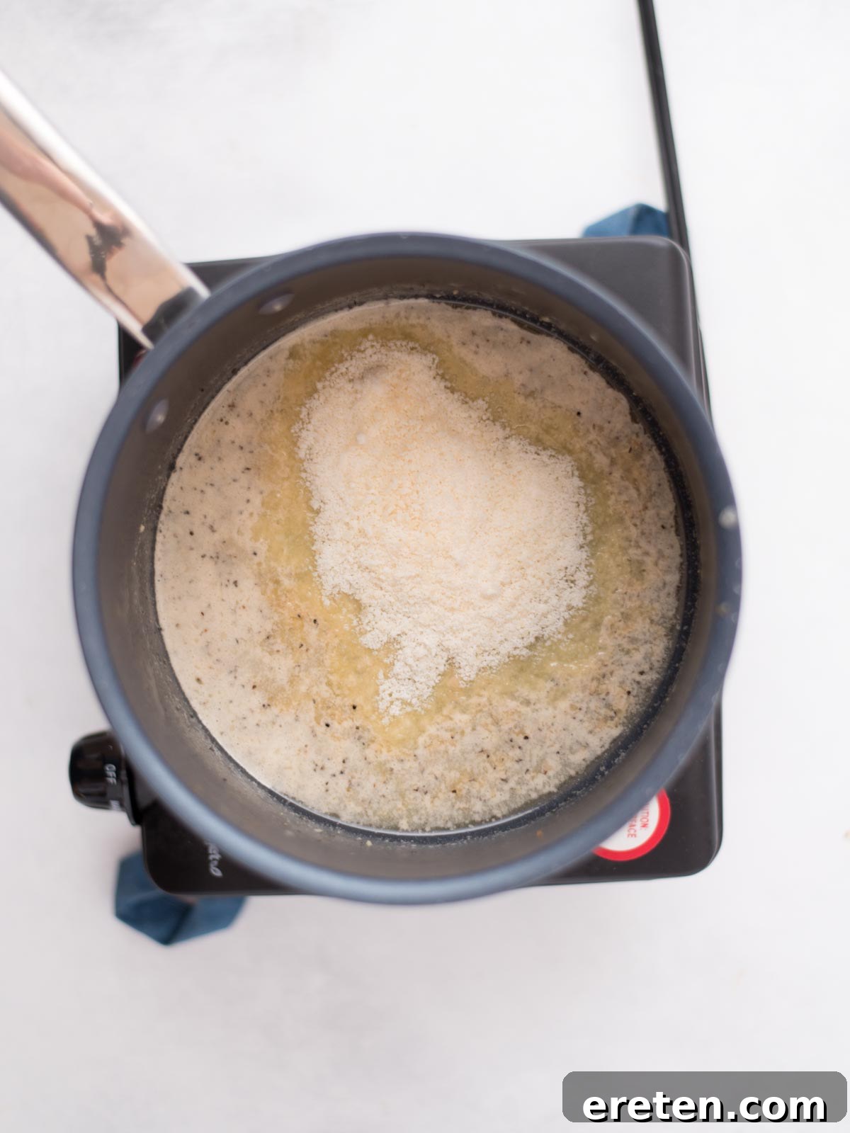 Air-Fried Golden Garlic Parmesan Wings 10 Grated parmesan cheese being added to the melted butter and garlic mixture in a saucepan, to form the sauce