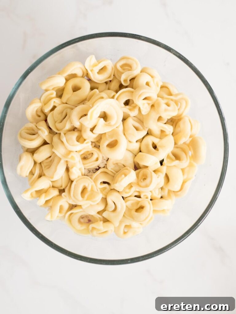 Mediterranean Tortellini Pasta Salad 9 Cooked and cooled tortellini being added to the bowl with vegetables and cheese.