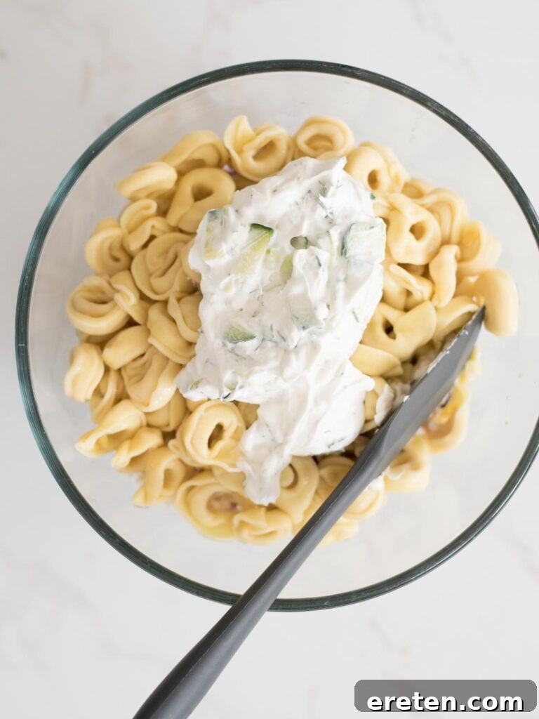 Mediterranean Tortellini Pasta Salad 10 Creamy tzatziki sauce being drizzled over the tortellini and other ingredients, ready for mixing.