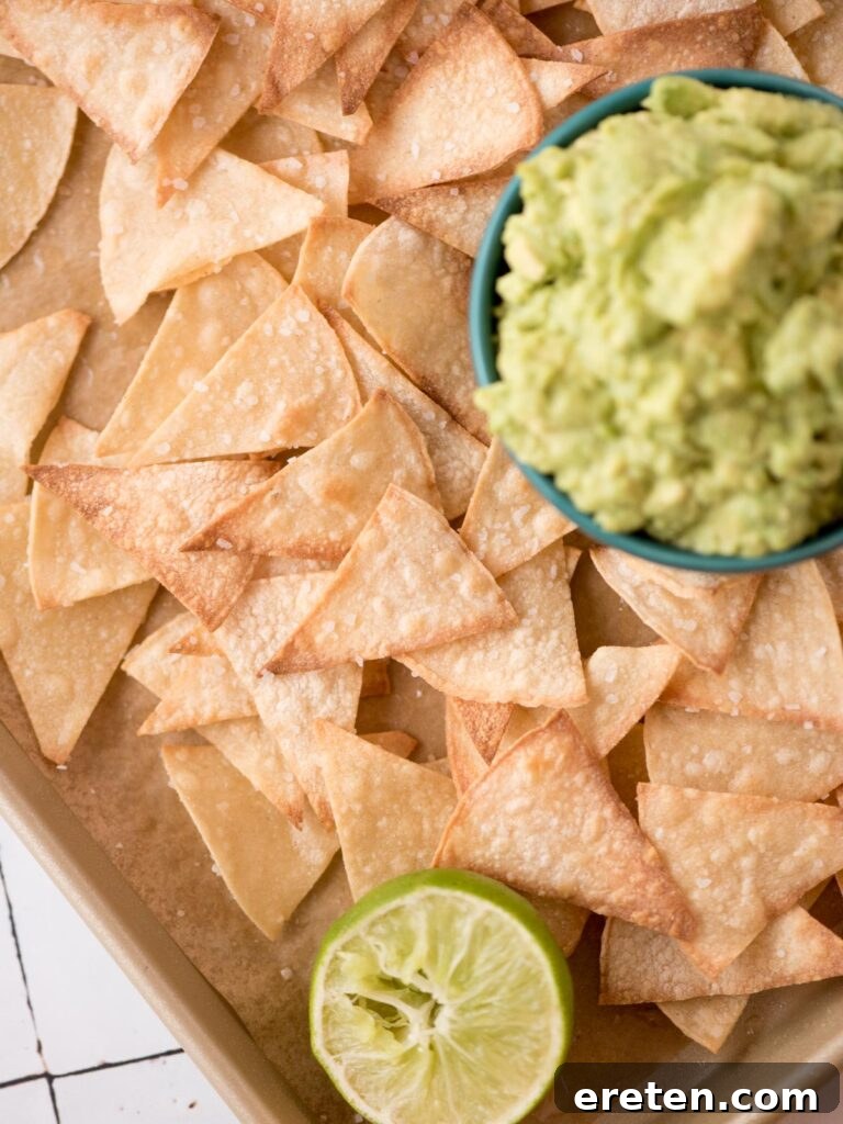 Small bowl of guacamole nestled in a tray of baked tortilla chips with a squeezed lime half.