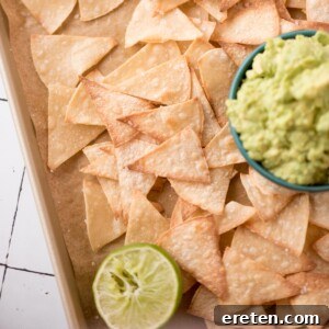 Delicious homemade baked chips on a serving tray with a side of guacamole and a squeeze lime half.