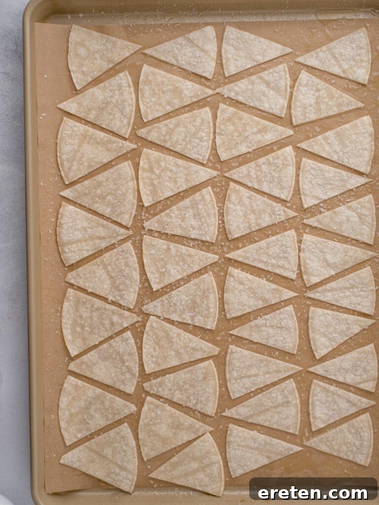 Baking tray with corn tortillas cut into triangle pieces, topped with avocado oil, salted and ready to bake.
