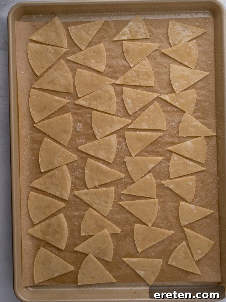 Salted and oiled corn tortillas cut into triangles on a baking sheet ready to bake.