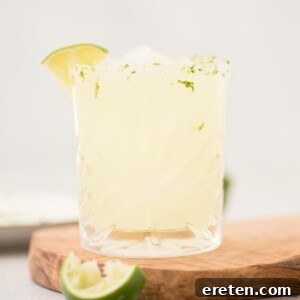 Stone Cold Margarita 6 margarita on the rocks in a glass that's lined with salt and lime zest on a wooden board with a lime wedge