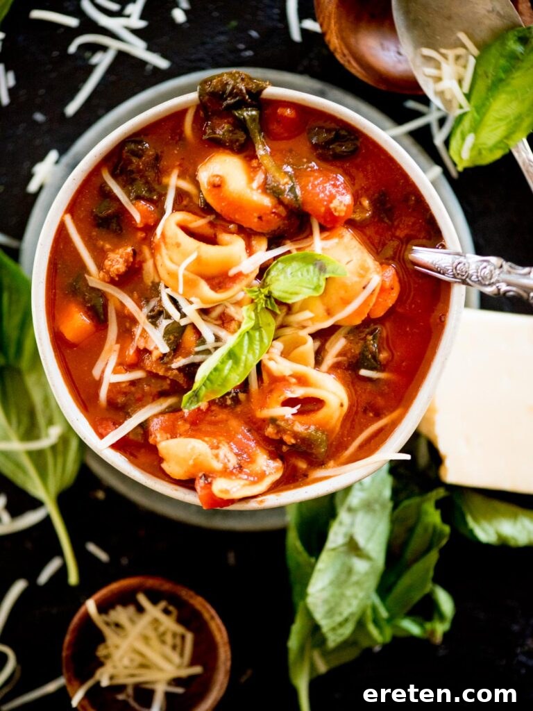 spinach tortellini soup in a bowl topped with grated parmesan and fresh basil