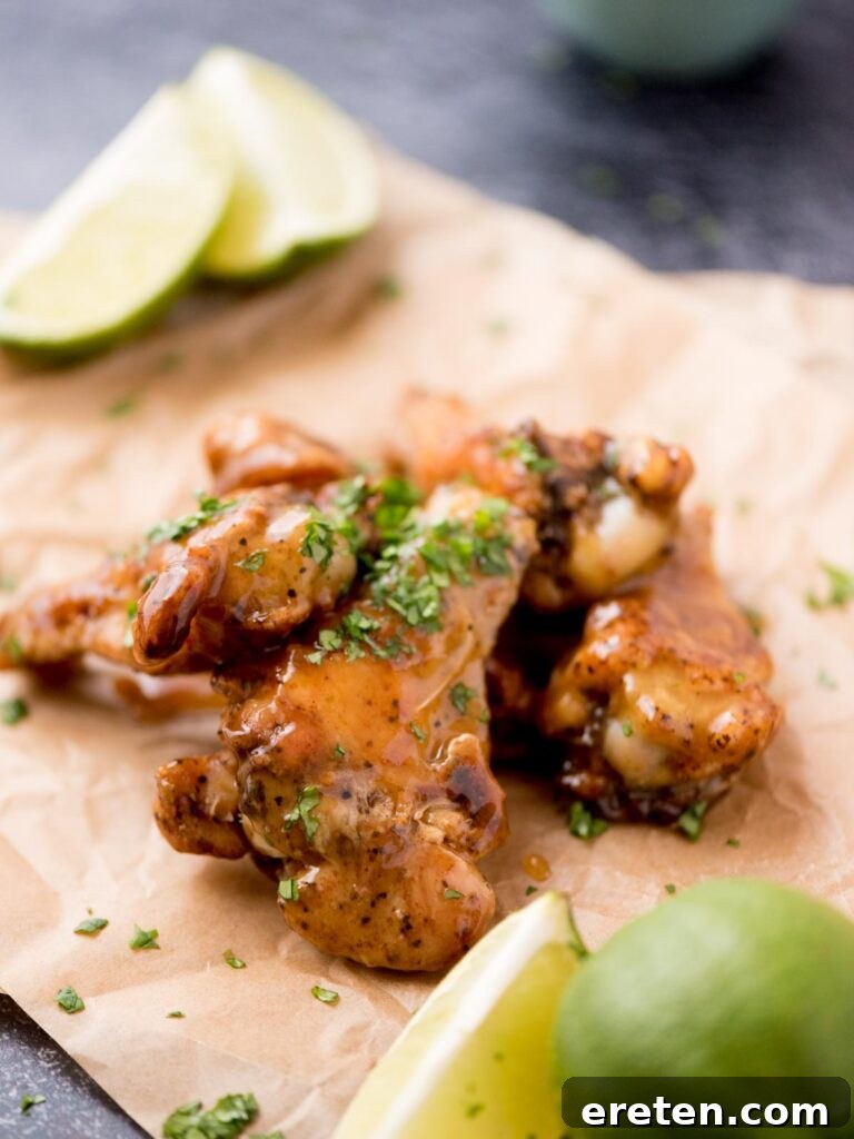 Fresh lime wedges on parchment paper next to a platter of glazed tequila lime wings.