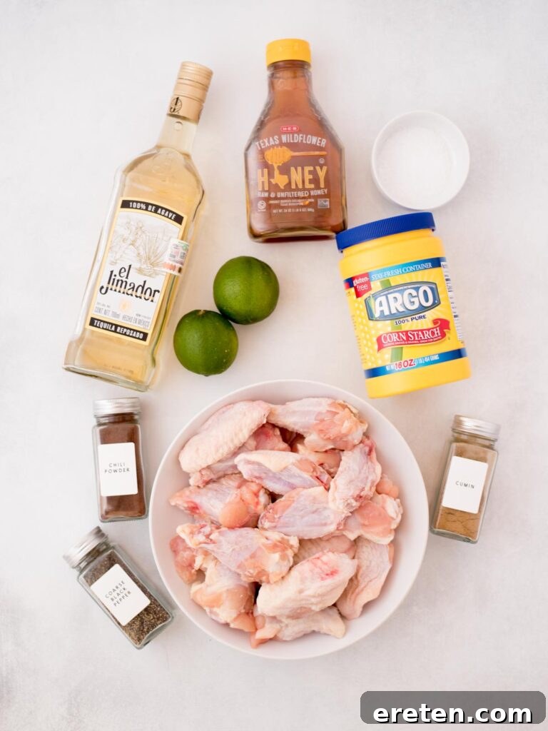 Assortment of fresh ingredients including limes, honey, spices, and a bottle of tequila, laid out for making the chicken wings.