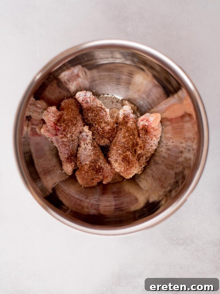 Raw chicken wings with seasonings added over them in a mixing bowl ready to combine.