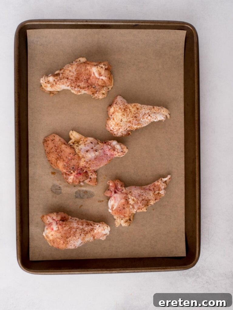 Seasoned raw chicken wings laying on parchment paper covered baking sheet.